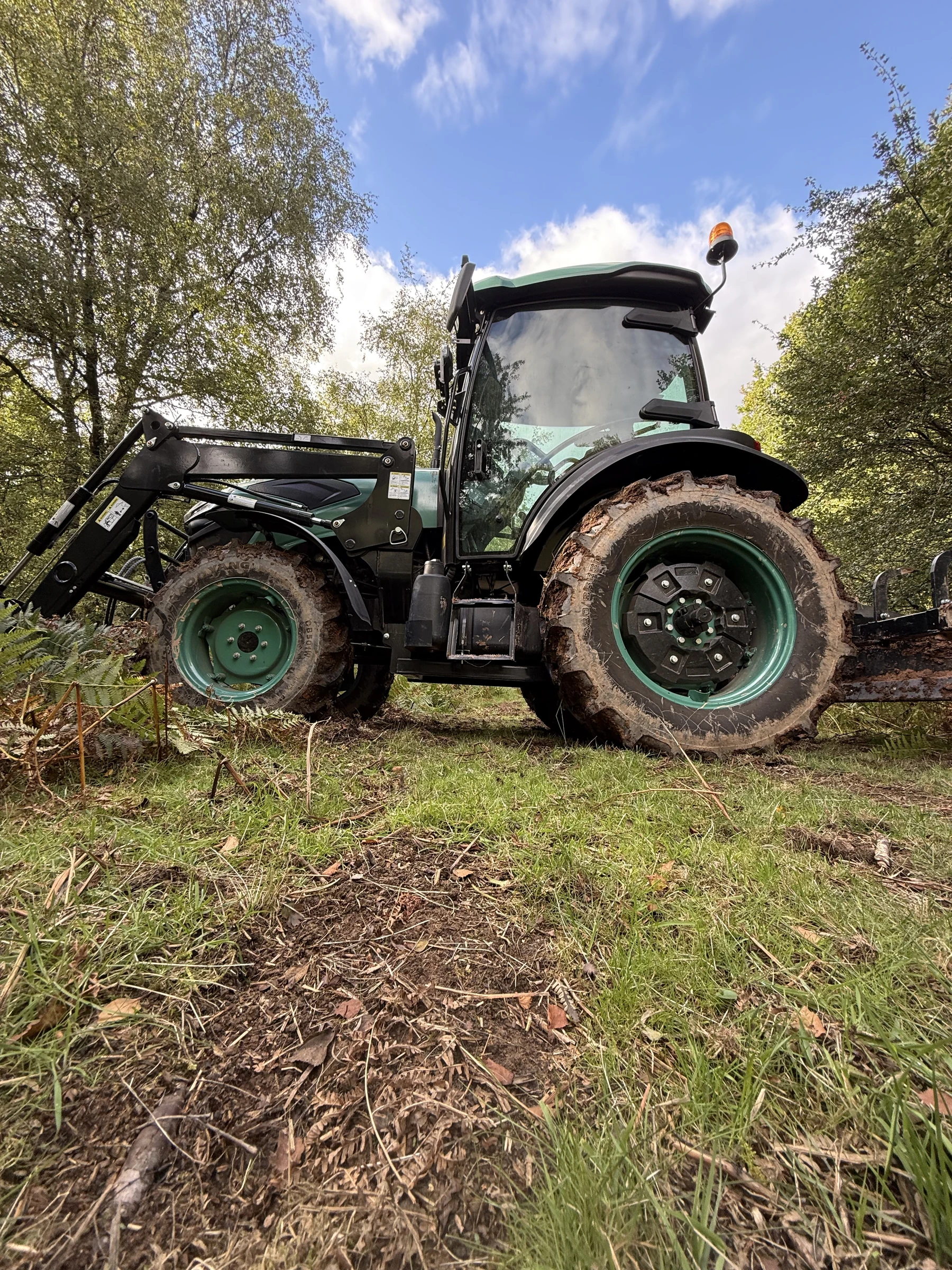 Side view of the BULL cab, HW Series 10 loader and mud-covered tyres on woodland ground