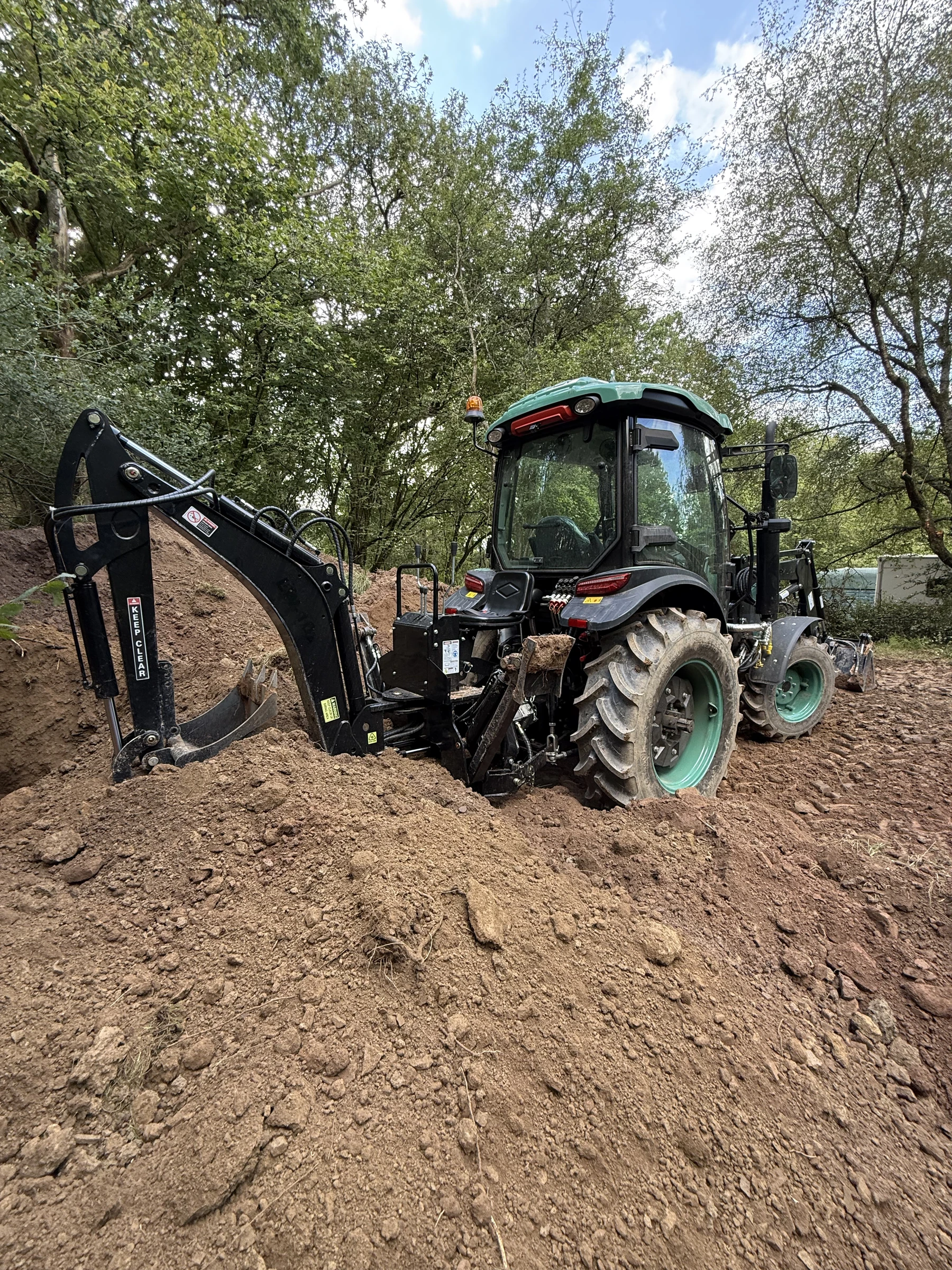 A closer rear view of the BULL and HW Series 10 backhoe beside freshly excavated woodland soil